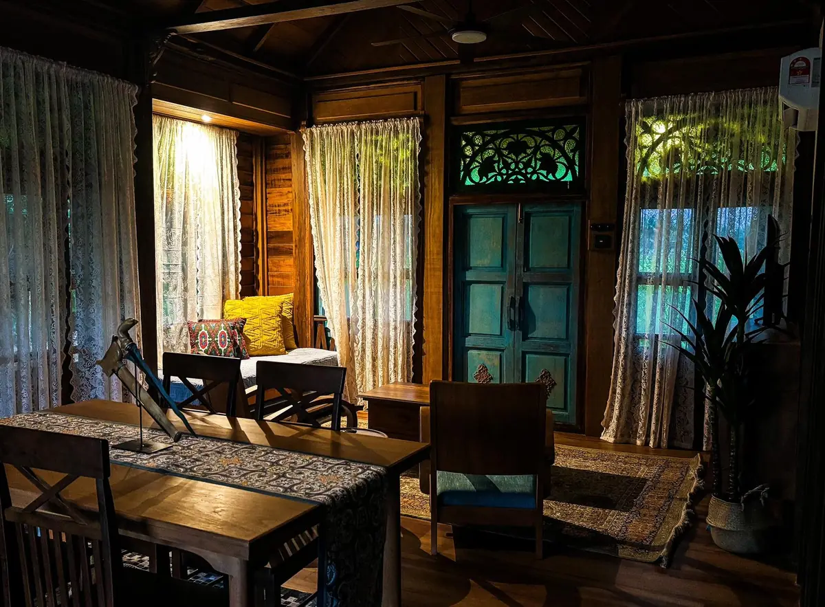 Living room with teak furniture, lace curtains, a keris on the table and carved green glass transom