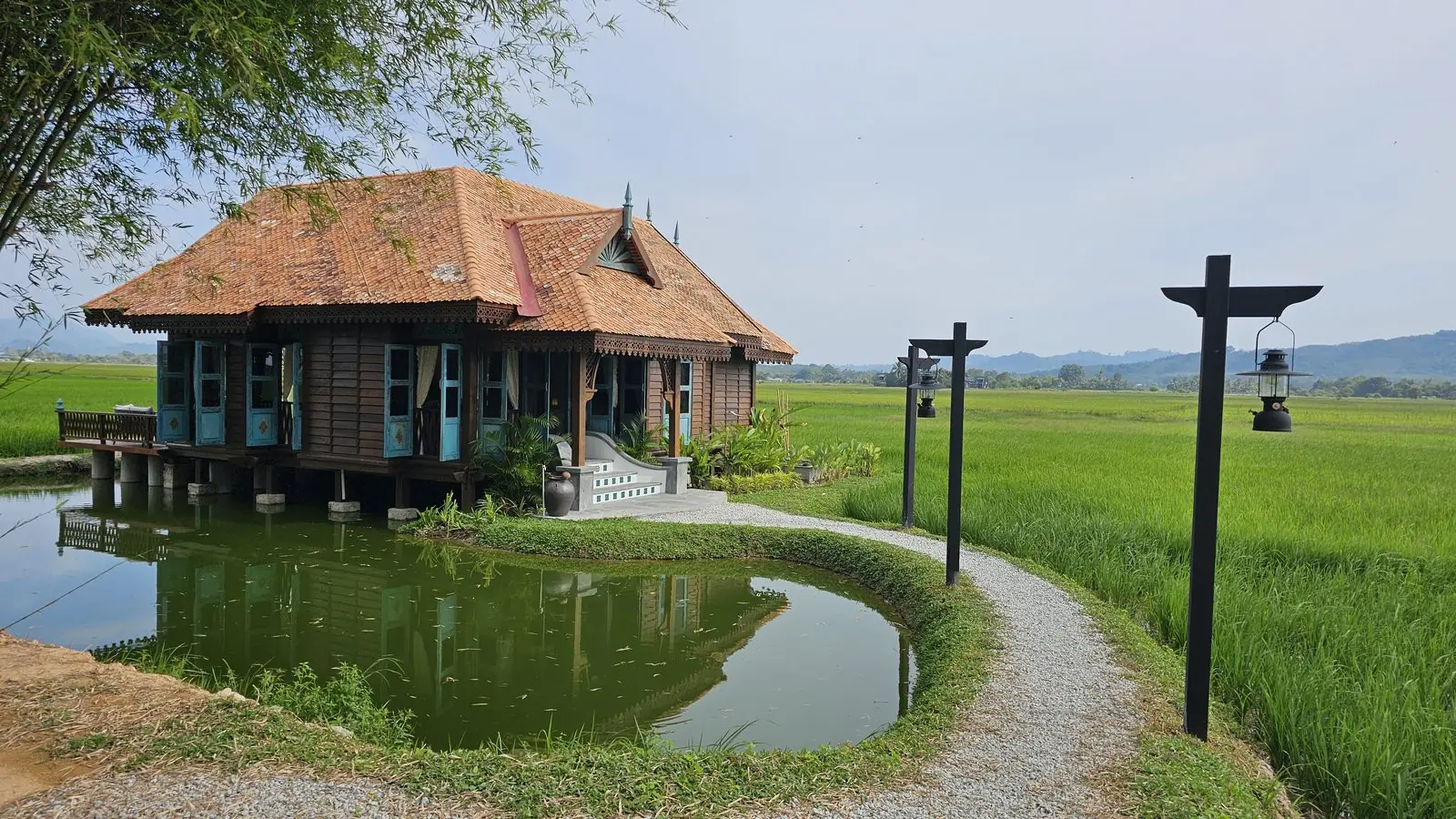 Rumah Uda, a timber house with turquoise doors over the fishing pond